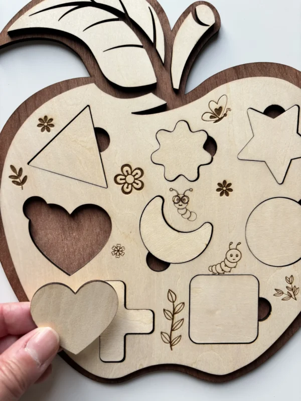 Puzzle en bois - Pomme - forme géométriques avec la pièce coeur tenue en main