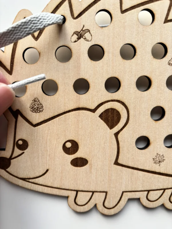 détail d'un hérisson à lacer en bois avec un lacet tenu en main