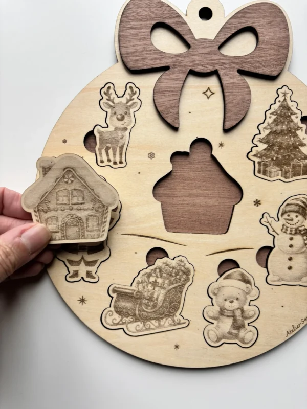 Puzzle en bois en forme de boule de noël - avec la pièce chalet tenue en main