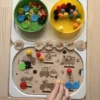 Insert sensoriel en bois avec véhicules gravés, jetons ronds et accessoires colorés et main d'enfant qui joue