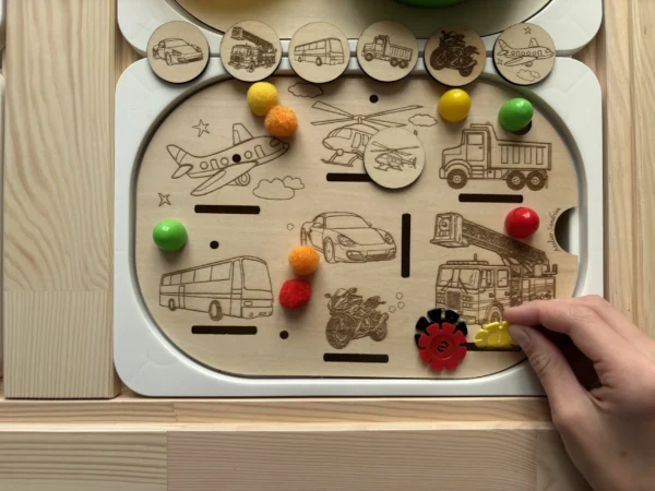 Insert sensoriel en bois avec véhicules gravés (version réaliste), jetons ronds et accessoires colorés à manipuler avec main d'enfant qui joue