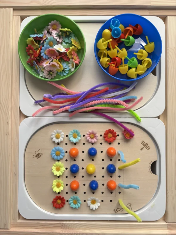 Insert sensoriel en bois forme carrée avec différents accessoires dans deux bols et accessoires posés sur l'insert