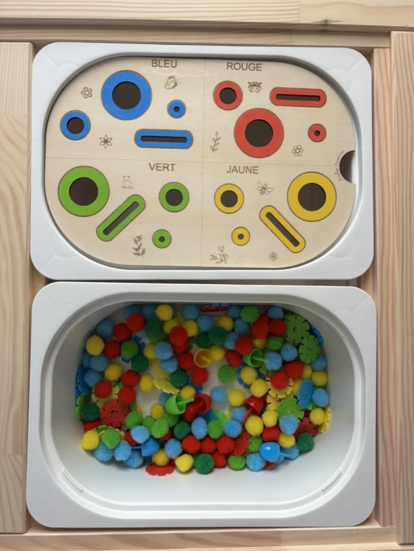 Insert sensoriel en bois avec fentes, trous picots et cercles de couleurs, avec pompons avec pompons, fleurs et picots dans un bac pour activité de tri et manipulation