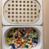 Insert sensoriel en bois avec trous pompons de 20 mm avec un bac rempli de pompons