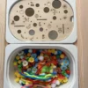 Insert sensoriel en bois avec trous de différentes tailles et illustrations gravées pour exploration et manipulation, un bac avec différents accessoires
