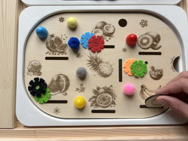 Enfant utilisant un insert sensoriel Fruits exotiques en bois avec pompons et jetons pour activité de tri et motricité fine
