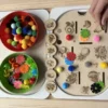 Enfant utilisant un insert sensoriel Fruits exotiques en bois avec pompons et jetons pour activité de tri et motricité fine