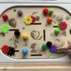 Enfant utilisant un insert sensoriel en bois fruits du verger avec pompons et fleurs pour motricité fine