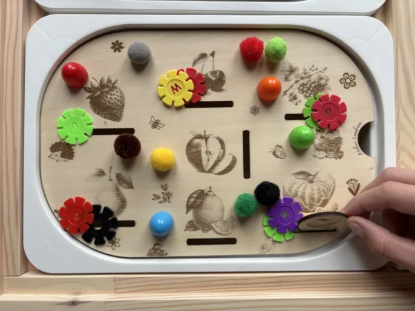 Enfant utilisant un insert sensoriel en bois fruits du verger avec pompons et fleurs pour motricité fine