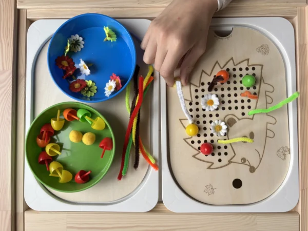 insert sensoriel en bois hérisson à petits trous avec chenilles et fleurs et bols accessoires et une main d'enfant qui joue