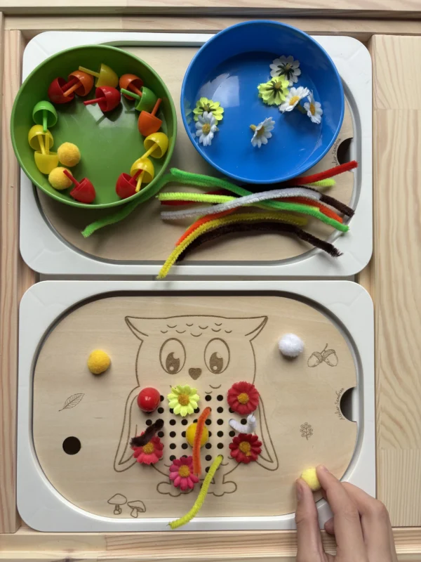 Main d’enfant utilisant un insert sensoriel hibou en bois avec pompons et fleurs pour la motricité fine
