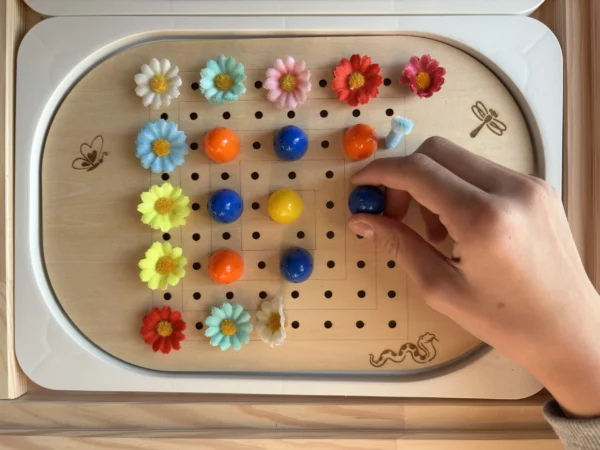 Insert sensoriel en bois forme carrée avec une main d'enfant qui joue et accessoires variés