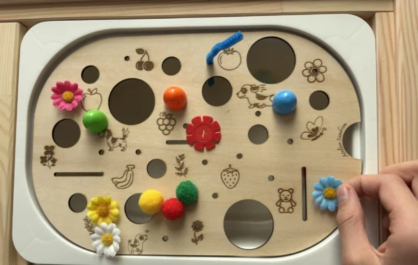 Insert sensoriel en bois à trous multiples avec motifs gravés avec accessoires variés et main d'un enfant