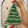 Insert sensoriel en bois - sapin rempli de pompons verts et quelques rouges avec une main d'enfant qui joue