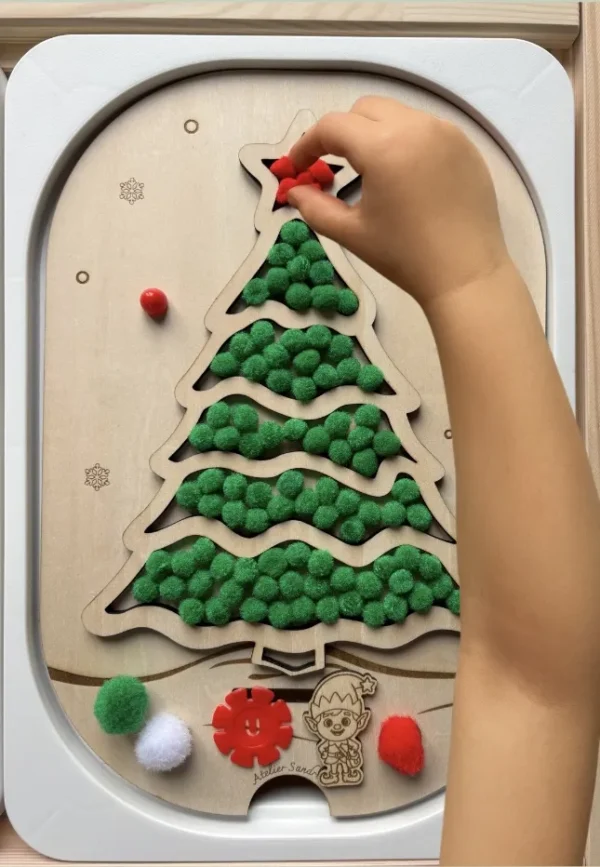 Insert sensoriel en bois - sapin rempli de pompons verts et quelques rouges avec une main d'enfant qui joue