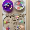 Enfant manipulant un insert sensoriel licornes en bois avec pompons et jetons pour activité de motricité fine