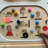Enfant manipulant un insert sensoriel en bois thème différents sports avec pompons et jetons colorés