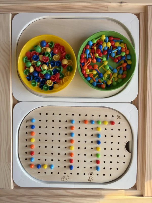 Insert sensoriel en bois avec trous picots plaque entière avec différents accessoires posés et dans deux bols et des picots posés sur l'insert qui forme le mot "lit"