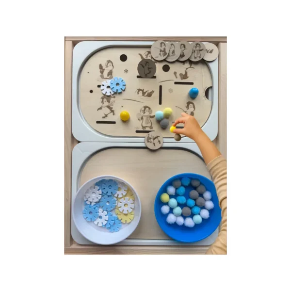 Main d’enfant manipulant un insert sensoriel pingouins en bois avec pompons et jetons pour motricité fine