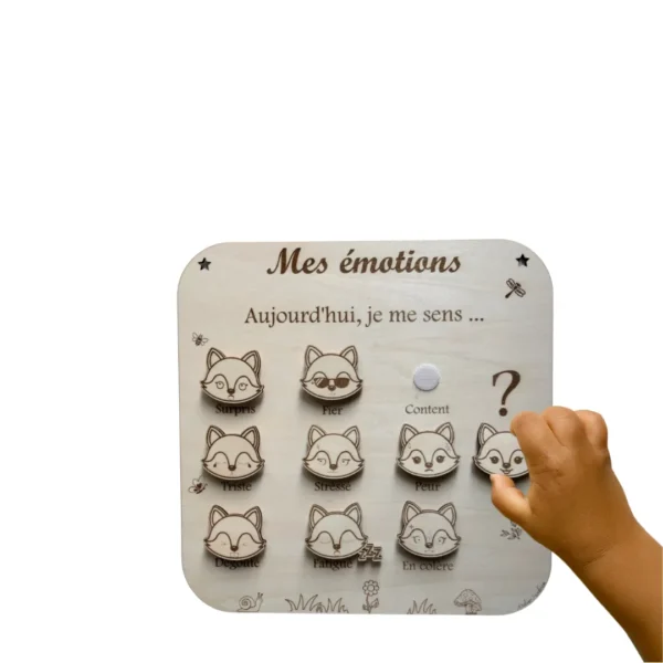 Main d’enfant plaçant un jeton sur le tableau éducatif en bois “Mes émotions” avec visages de renard pour exprimer ses ressentis