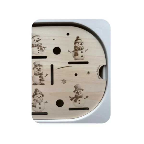 Détail d’un insert sensoriel en bois représentant des bonhommes de neige, avec fentes et trous pour activités de manipulation et motricité fine.