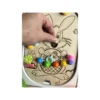 Main d’adulte manipulant un insert sensoriel en bois thème lapin de Pâques avec pompons colorés, favorisant la motricité fine et l’exploration sensorielle chez l’enfant.