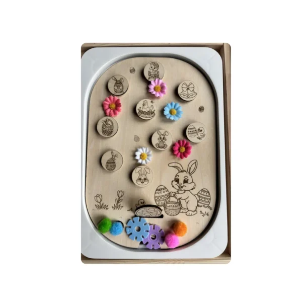 Insert sensoriel en bois thème Pâques décoré avec jetons illustrés, fleurs, pompons et accessoires colorés, activité créative favorisant la motricité fine et l’imagination des jeunes enfants.