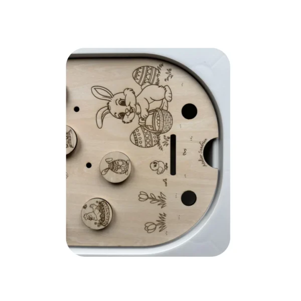 Insert sensoriel en bois gravé représentant un lapin de Pâques entouré d’œufs décorés, avec jetons illustrés pour activités de tri et motricité fine chez l’enfant.
