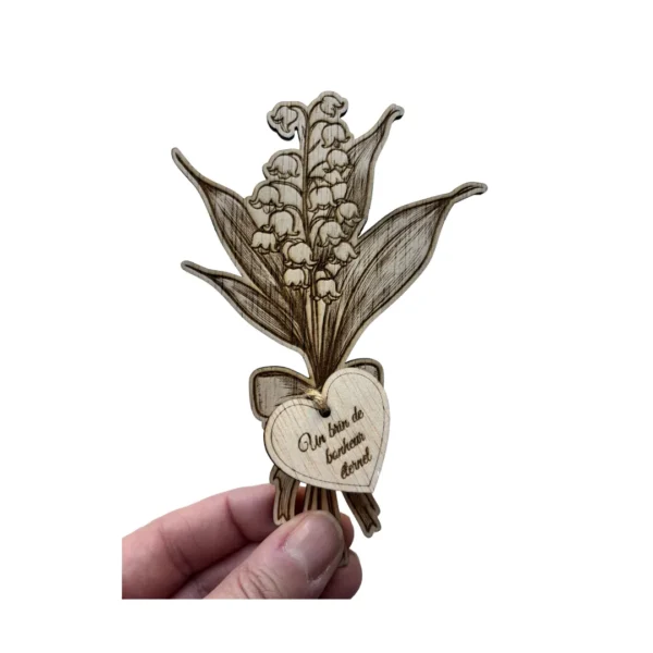 Brin de muguet en bois avec étiquette cœur gravée tenu dans une main