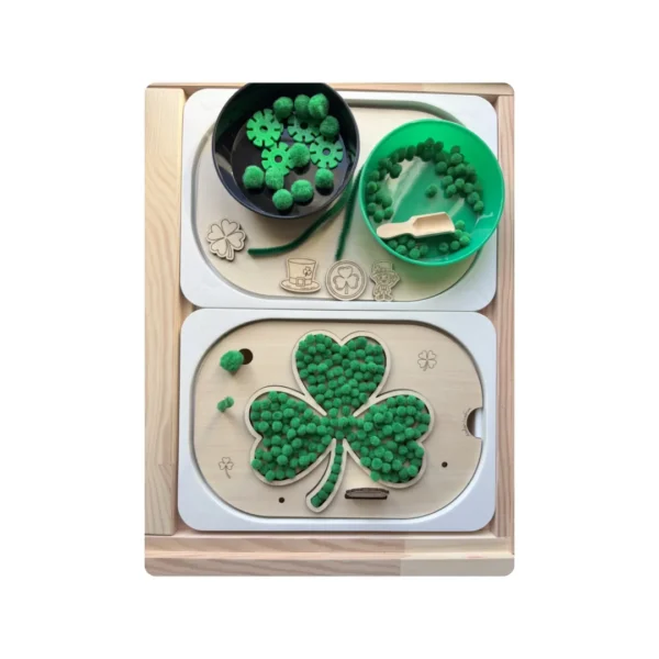 Insert sensoriel en bois trèfle Saint-Patrick avec bols et accessoires verts et pompons verts pour activité de motricité fine.